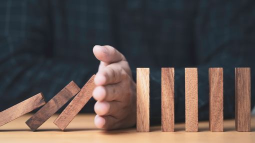 Image of a hand blocking the falling wooden dominos.
